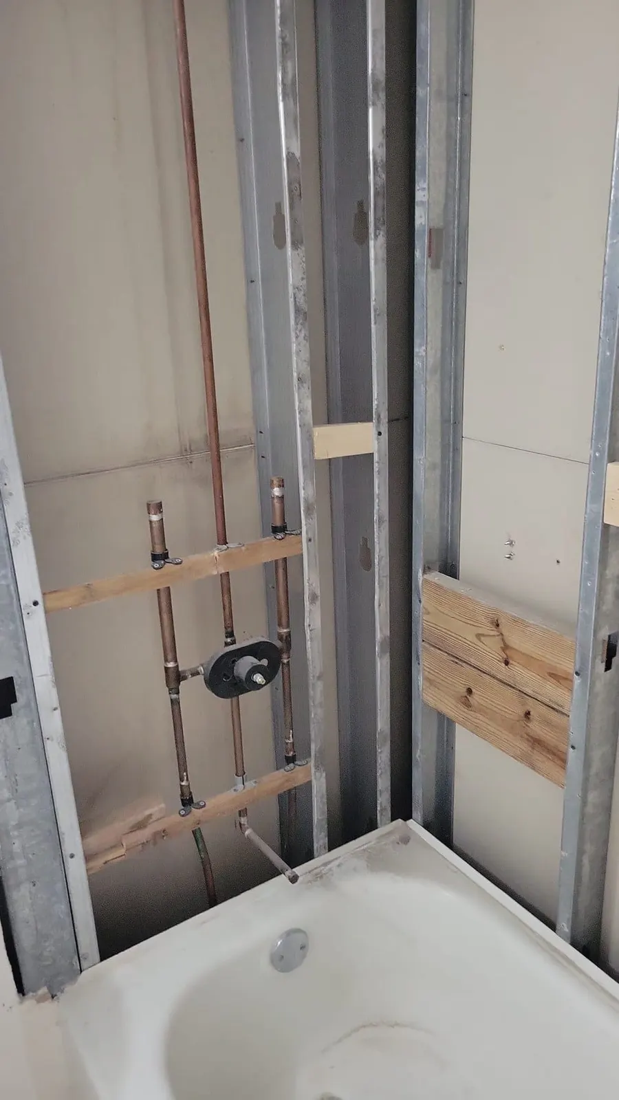 Bathtub area during renovation with exposed studs and visible plumbing.