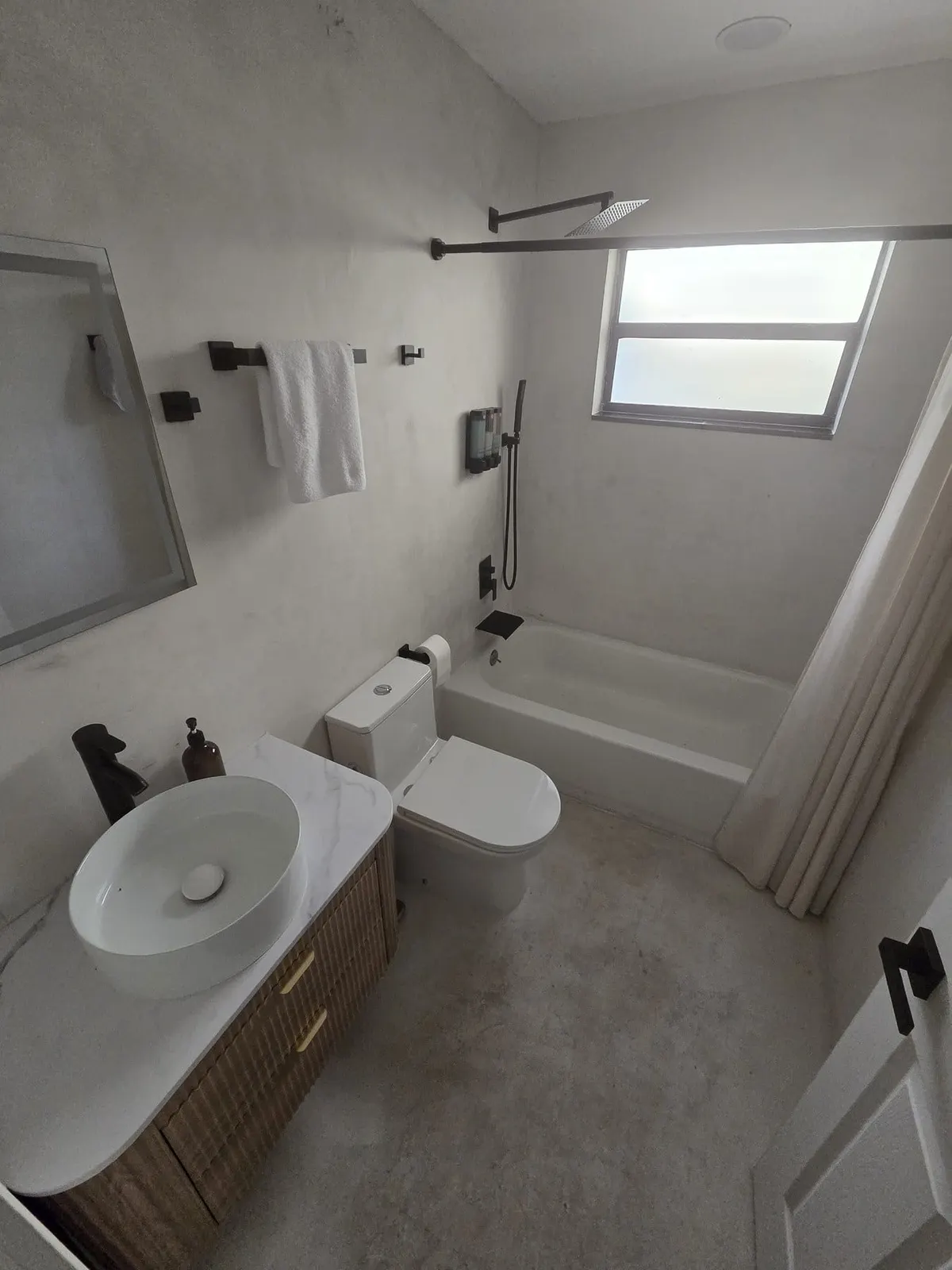 Compact bathroom with round vessel sink, toilet, and light gray tile walls.